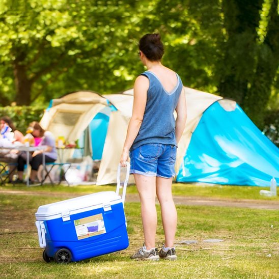 Femme portant une glacière à roulettes dans un camping, idéale pour conserver vos aliments.